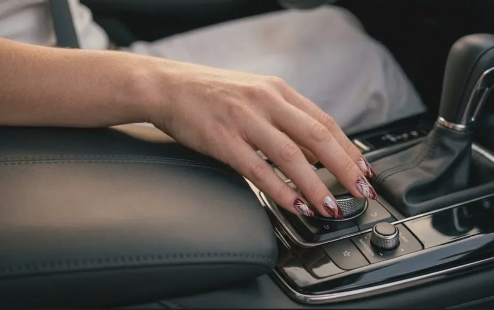 Detailed shot of a fresh gel manicure on medium-length almond nails operating the center console rotary dial in a Mazda CX-30.