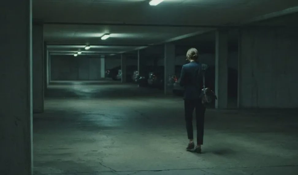 A large, empty underground parking garage features a woman dressed in dark business-casual attire.